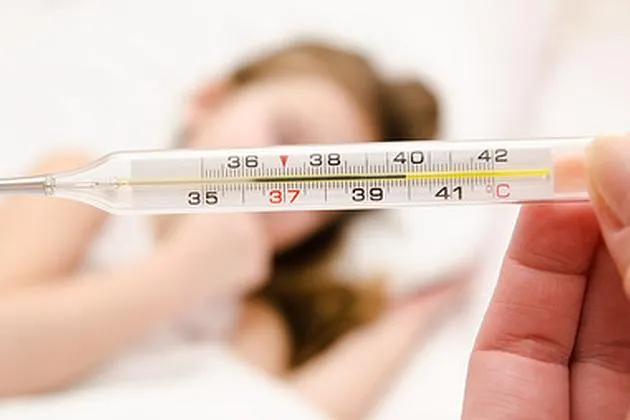 Mother holding thermometer foreground and sick little girl